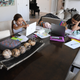 Two young girls sit at a dining room table working on their computers for remote learning during a lockdown.